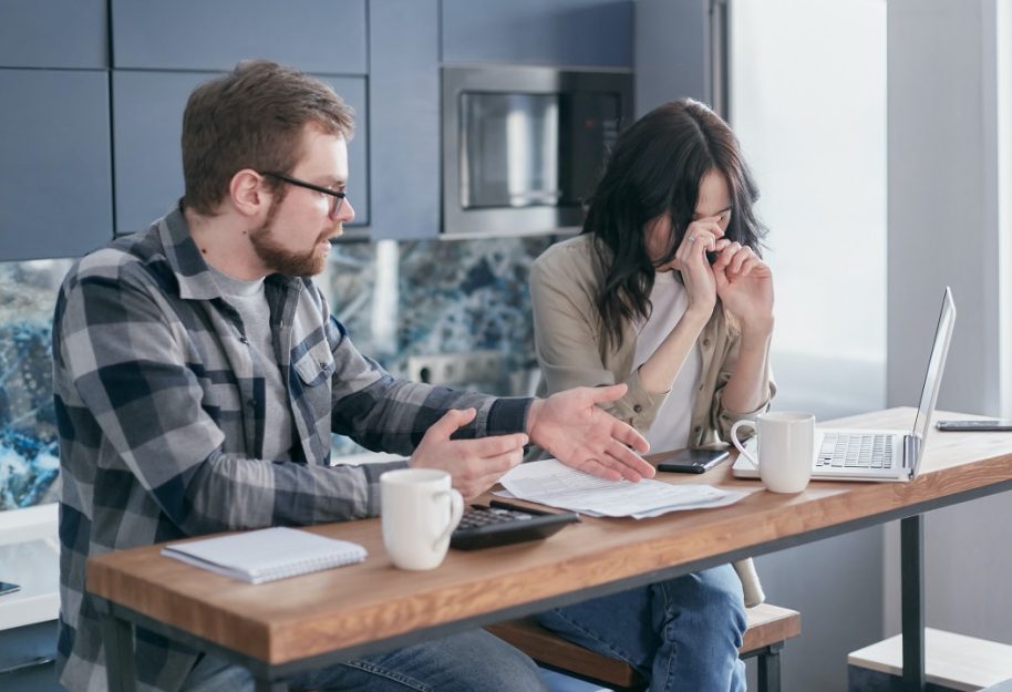 Two people sit at a desk working, they look stressed and frustrated.